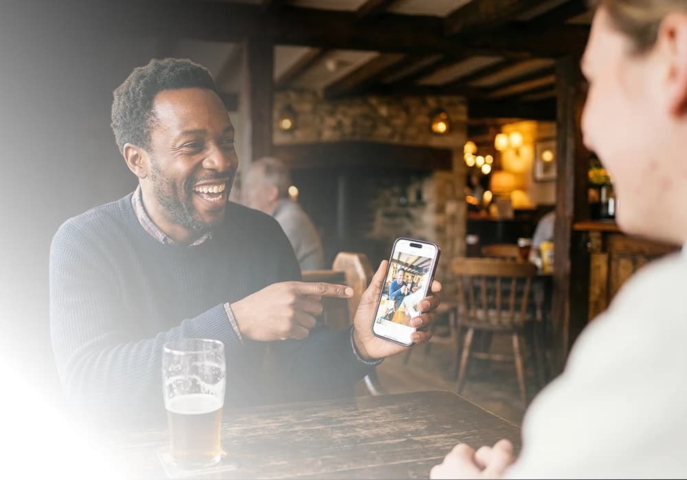 Two friends sharing a drink in a pub while one shows the other the Purple app