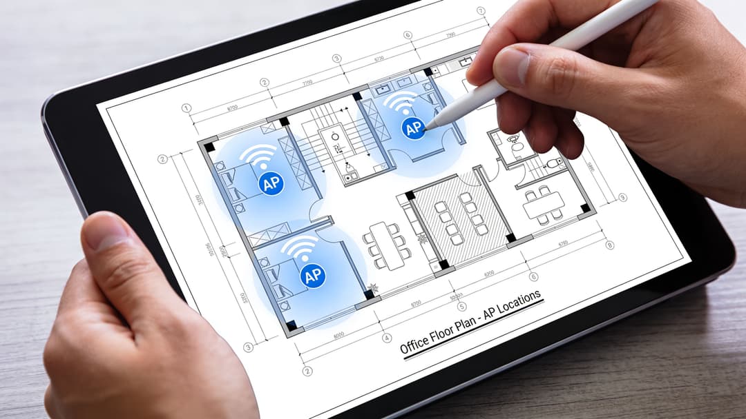 A person uses a digital stylus on a tablet showing an office floor plan with wireless access points.